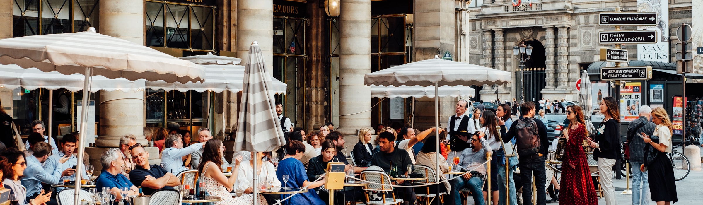 A Paris street with café terraces and people relaxing at outdoor tables.